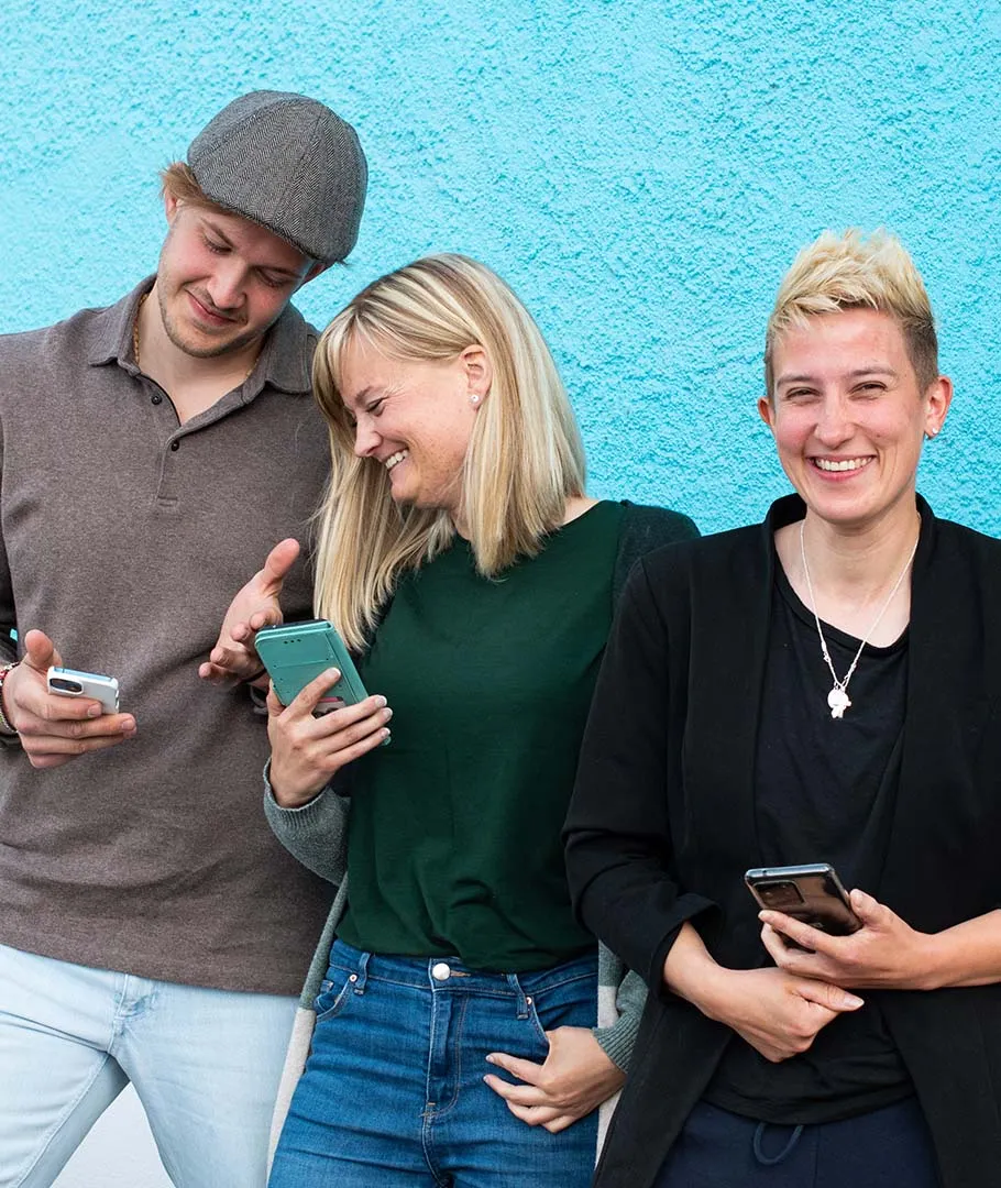 Drei junge Erwachsene lachen gemeinsam vor einer blauen Wand